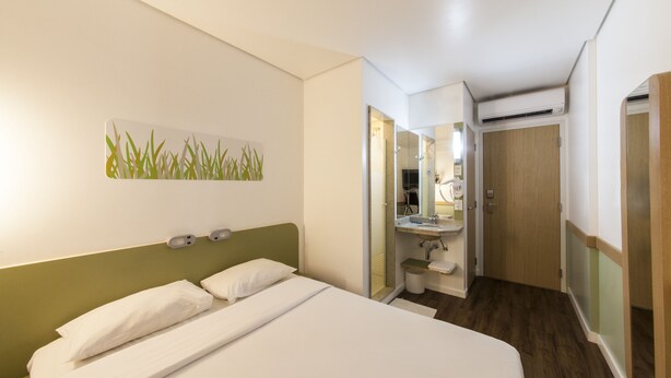 A hotel room with a bed, a bedside table, a mirror, a sink, and a door leading to another room. - ibis budget Manaus (Manaus)