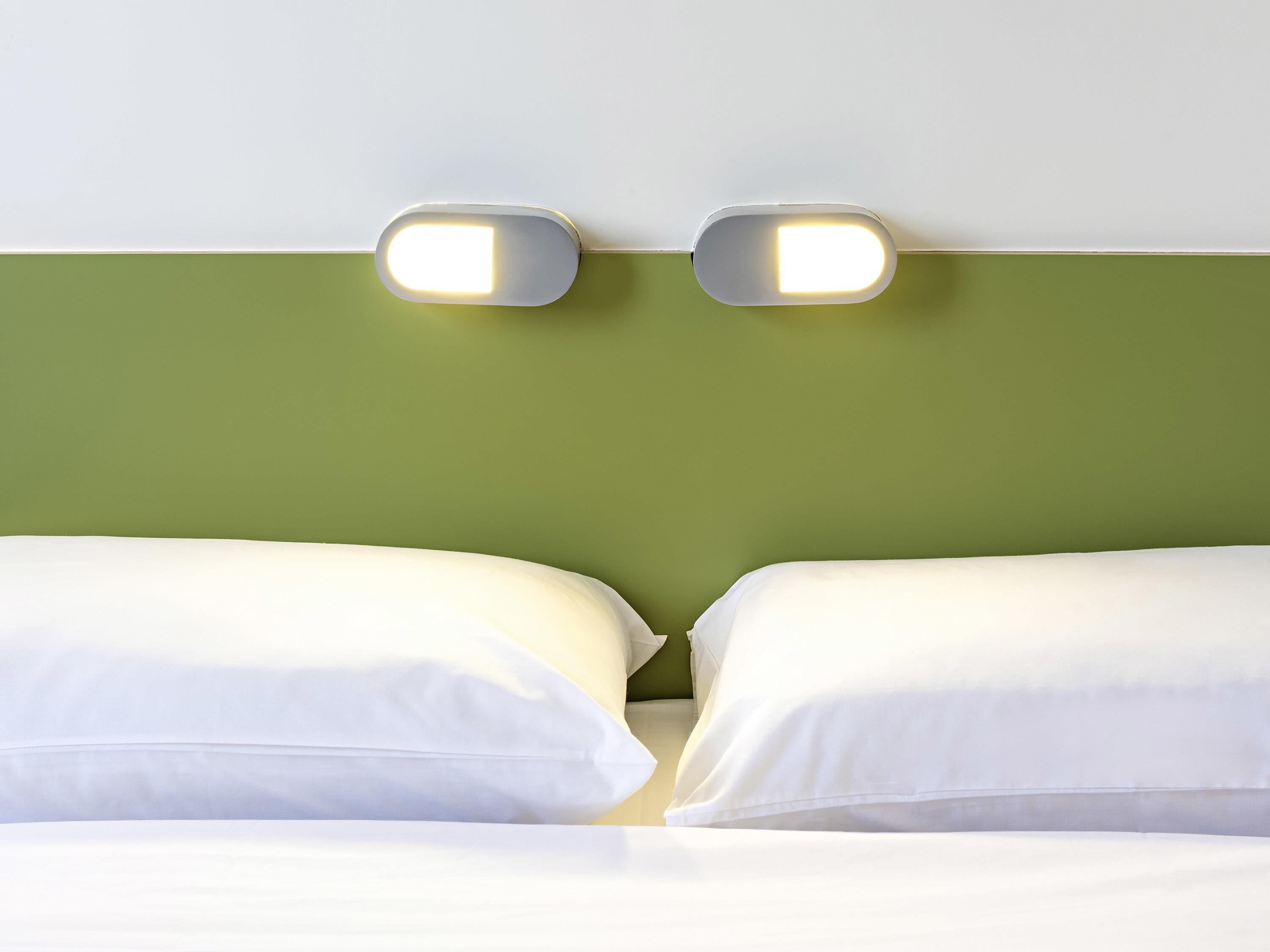 A bed with white bedding and two illuminated wall-mounted light fixtures.