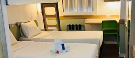 A compact hotel room with two beds, a small kitchenette, a television, and a window with curtains.