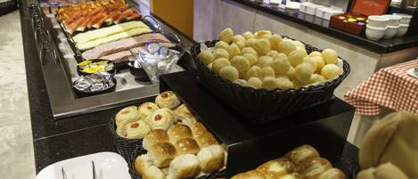 Un buffet proposant une variété d’aliments, notamment du pain, des pâtisseries et un grand panier rempli de petits pains ronds.