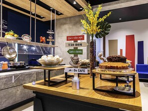 Una barra de café con diversos productos de pastelería, una máquina de café y una planta decorativa.