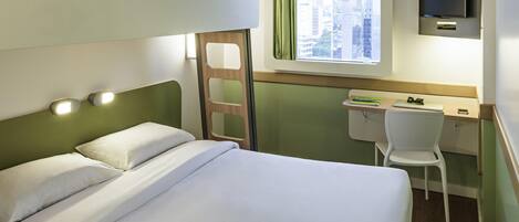Una cama individual con escritorio y silla, un televisor y una ventana con vistas a la ciudad.