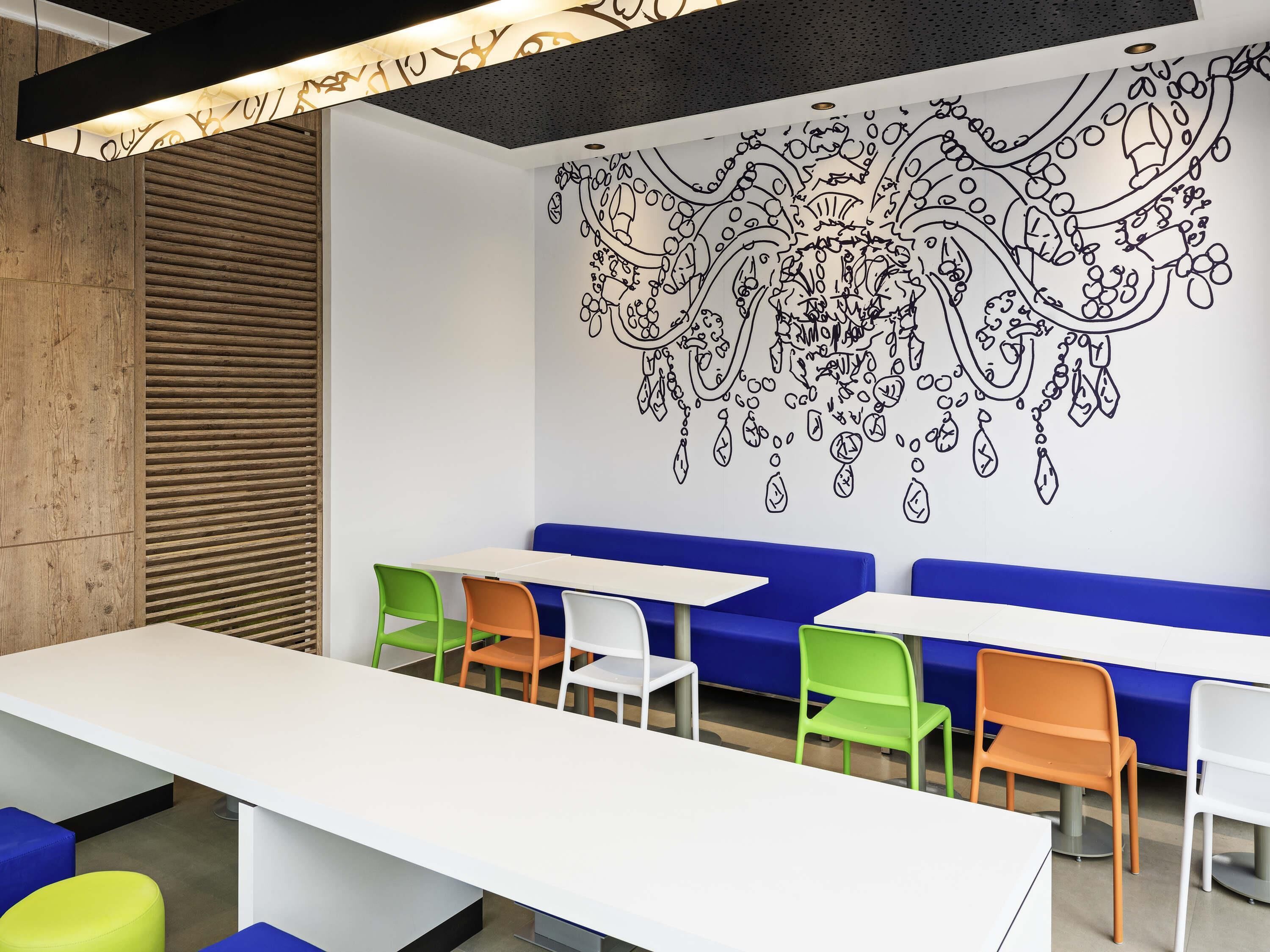 A modern interior with a white table, colorful chairs, and a wall mural.