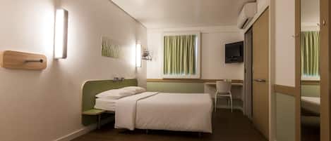 A hotel room with a bed, a desk, a chair, a television, and a wardrobe.