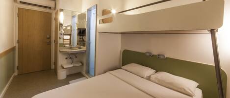 A compact hotel room with a bunk bed, a small bathroom with a sink, and a mirror.