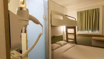 Ein Hotelzimmer mit Etagenbett, einem kleinen Badezimmer mit Toilette und Waschbecken sowie einem Fenster mit Vorhängen.