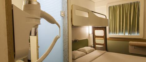 A hotel room with a bunk bed, a small bathroom with a toilet and sink, and a window with curtains.