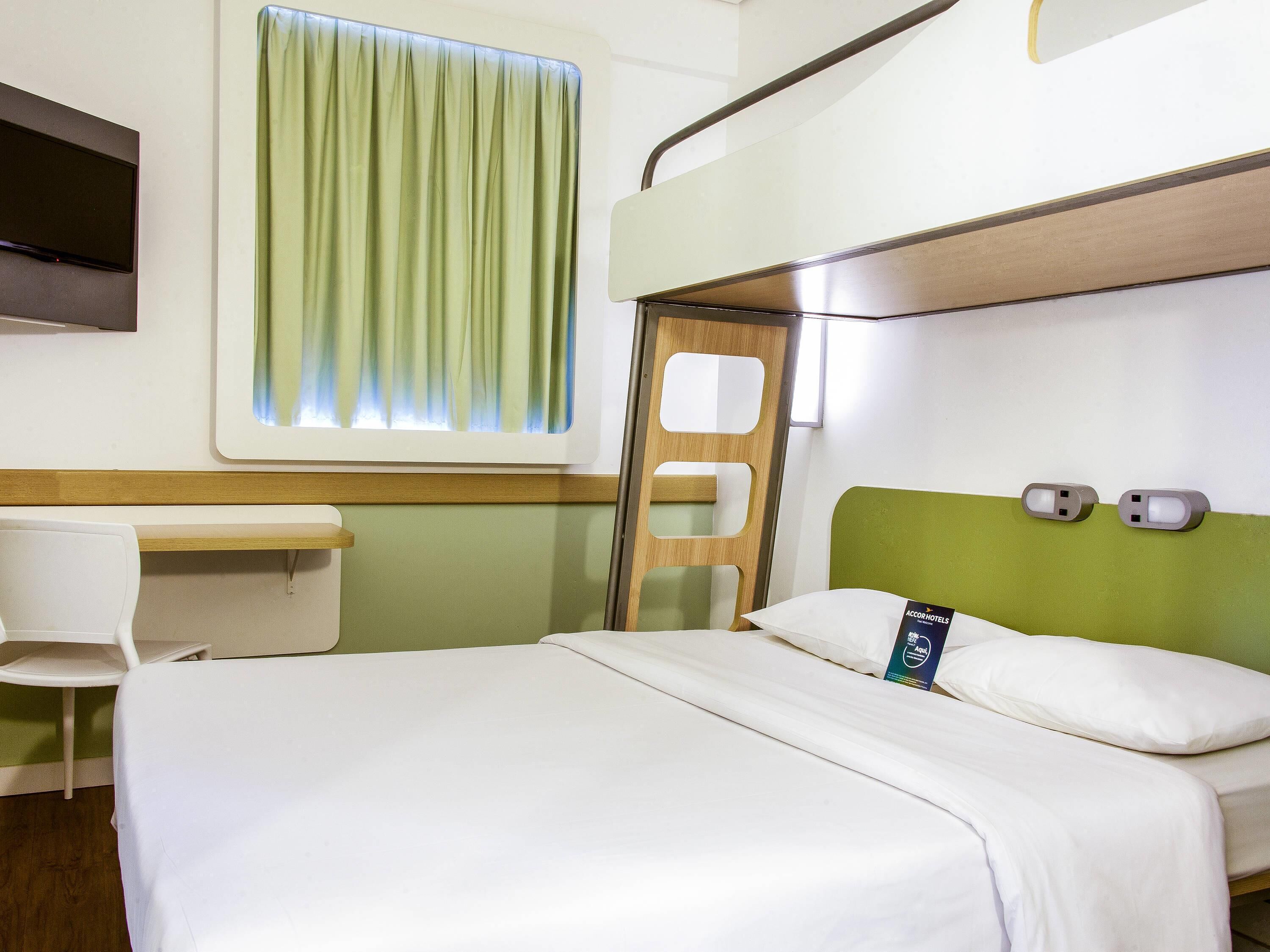 A hotel room with a bed, a desk, a chair, a TV, and a window with curtains.