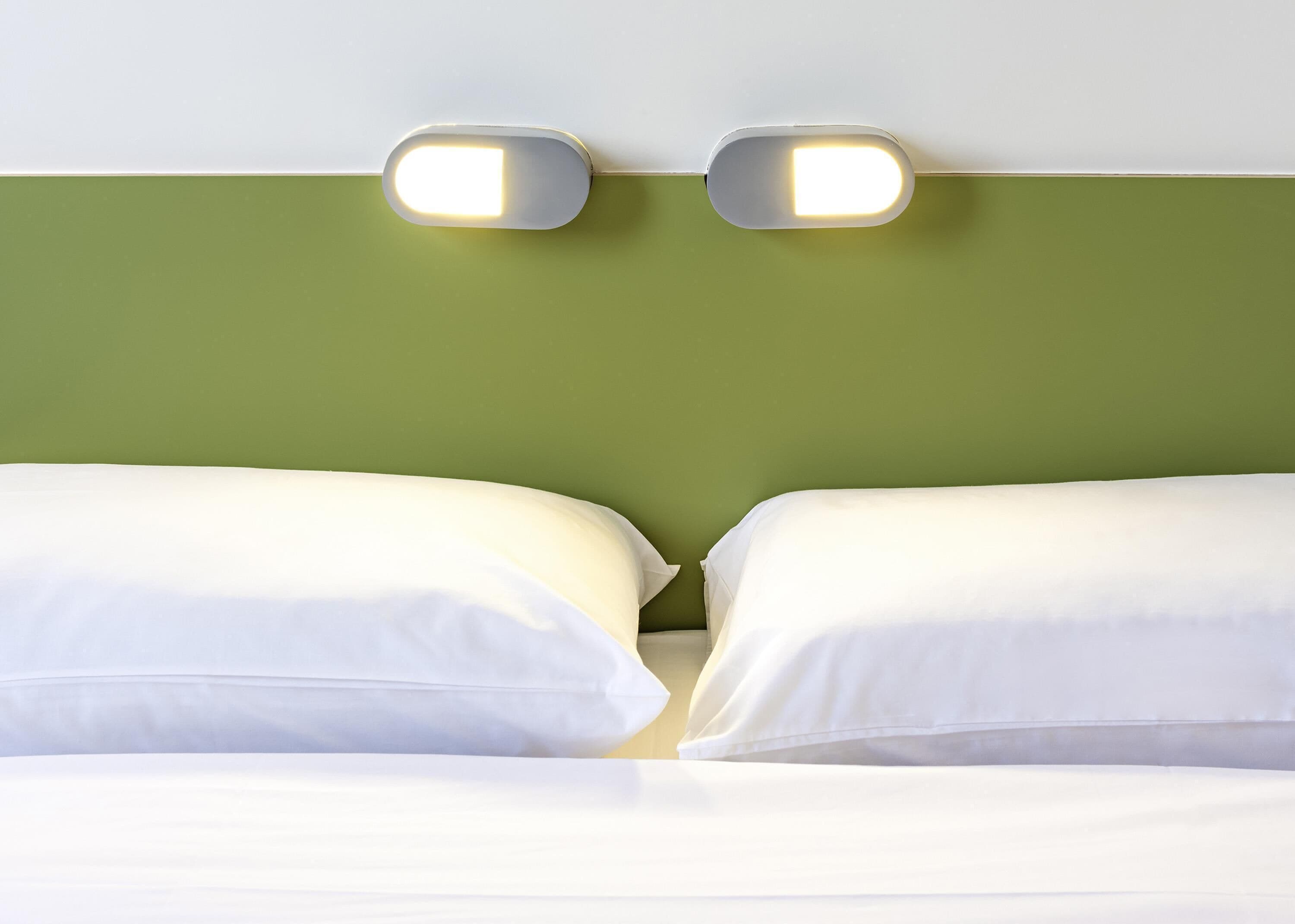 Un lit avec du linge de lit blanc et deux lampes fixées au mur au-dessus.