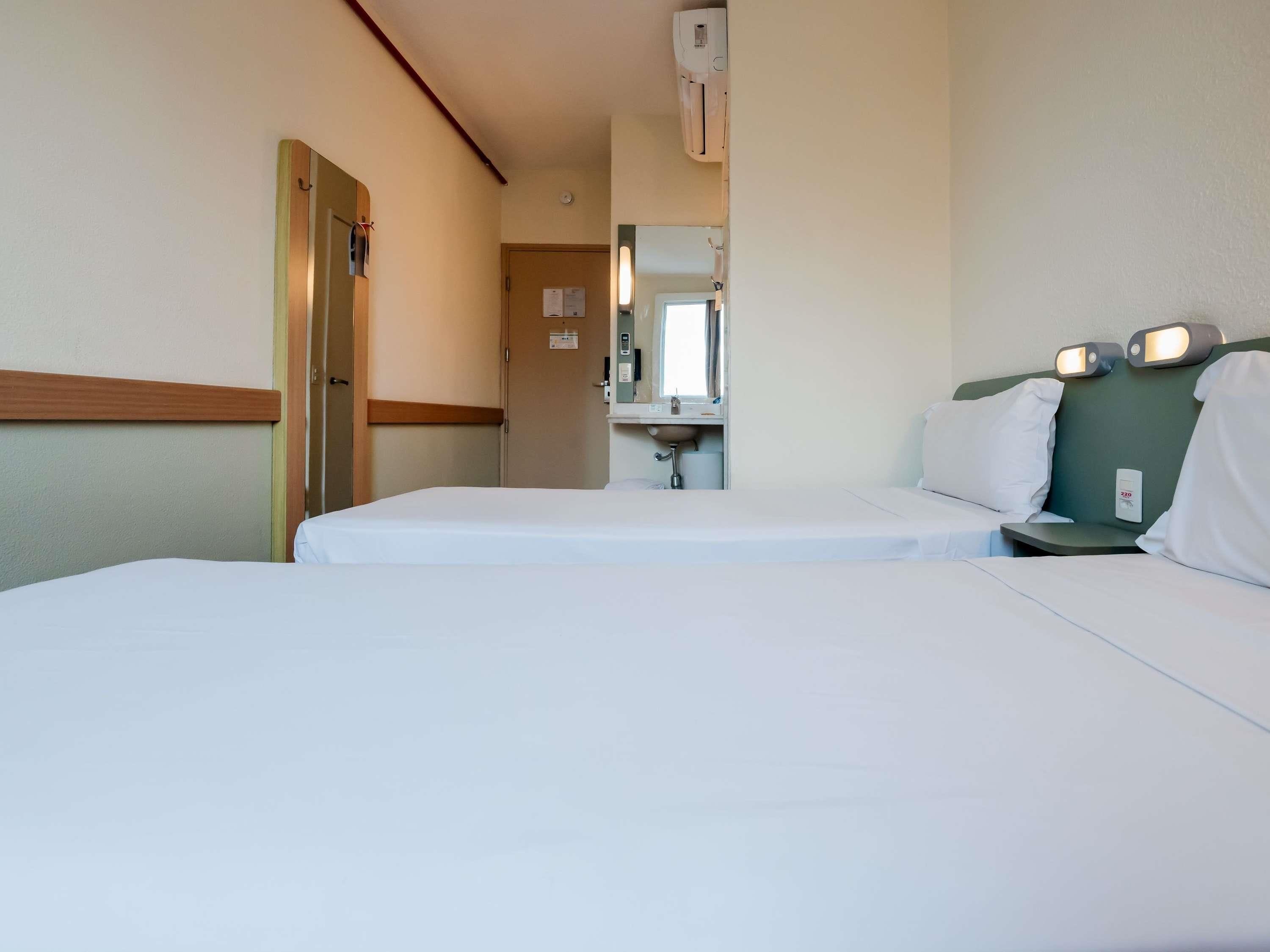 A hotel room with a bed, bedside table, and a mirror.