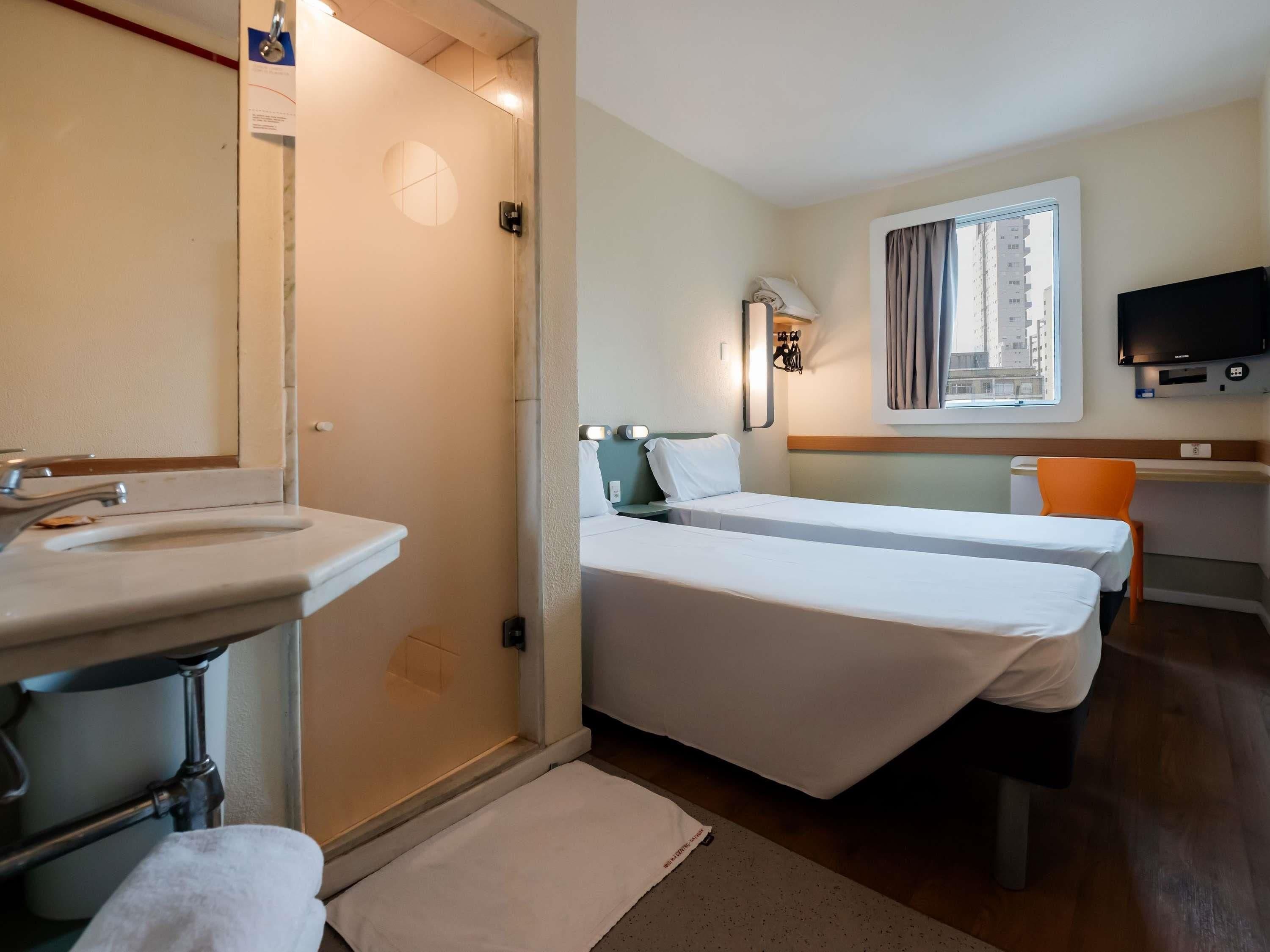 Habitación de hotel con baño, cama, escritorio y televisor.