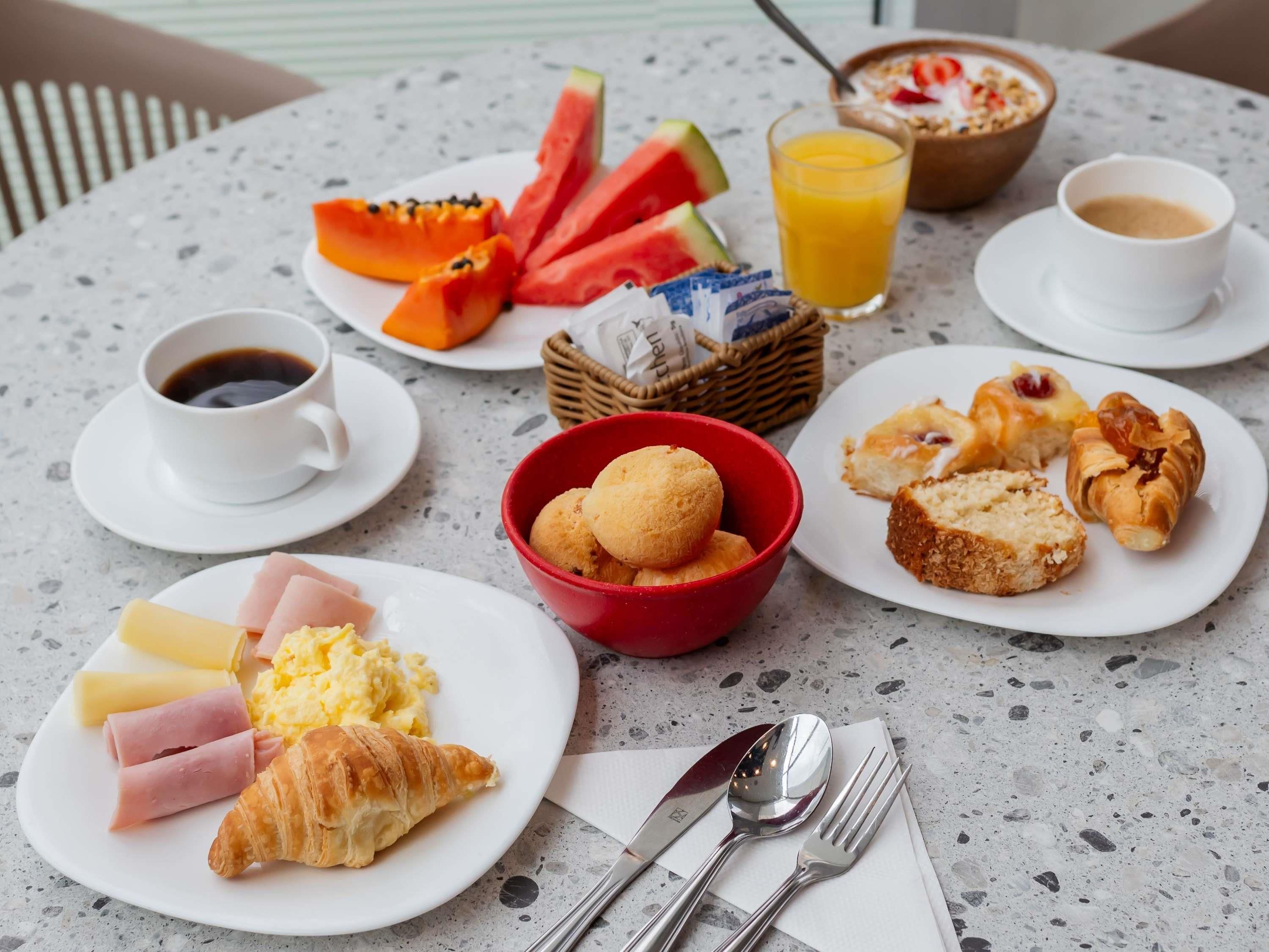 Een ontbijttafel met borden eten, een broodmand, een glas jus d'orange, een kop koffie en een kom brood.