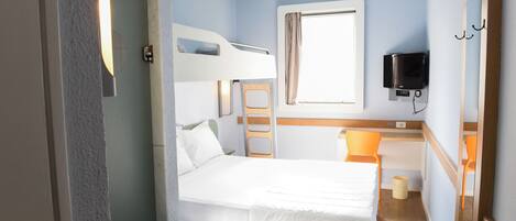 A compact room with a bunk bed, a desk with a chair, a television mounted on the wall, and a window with curtains.