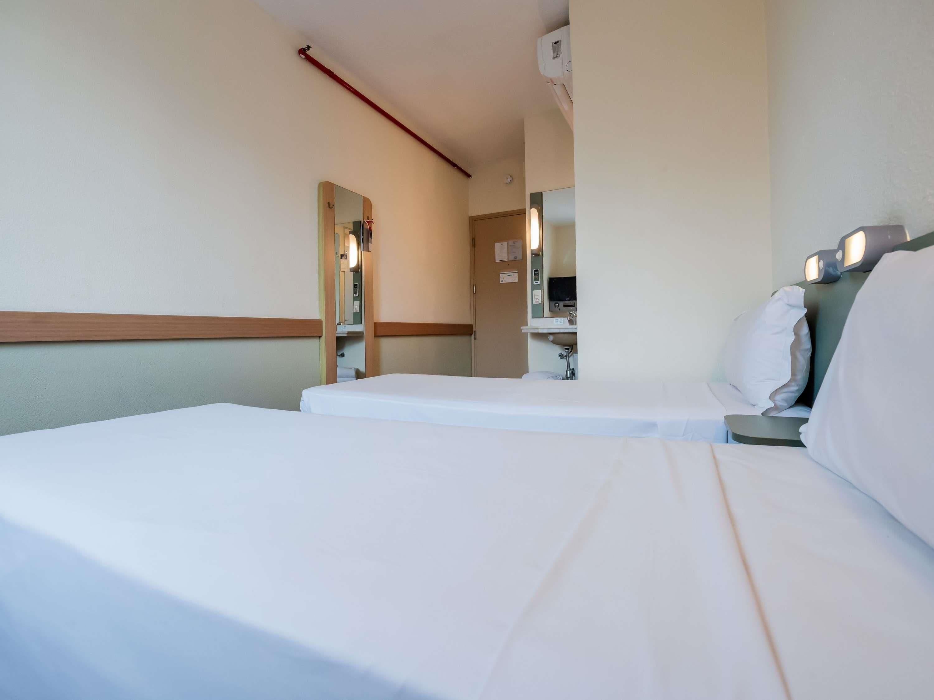 Une chambre d’hôtel équipée d’un lit, d’une table de chevet, d’un miroir et d’un climatiseur fixé au mur.