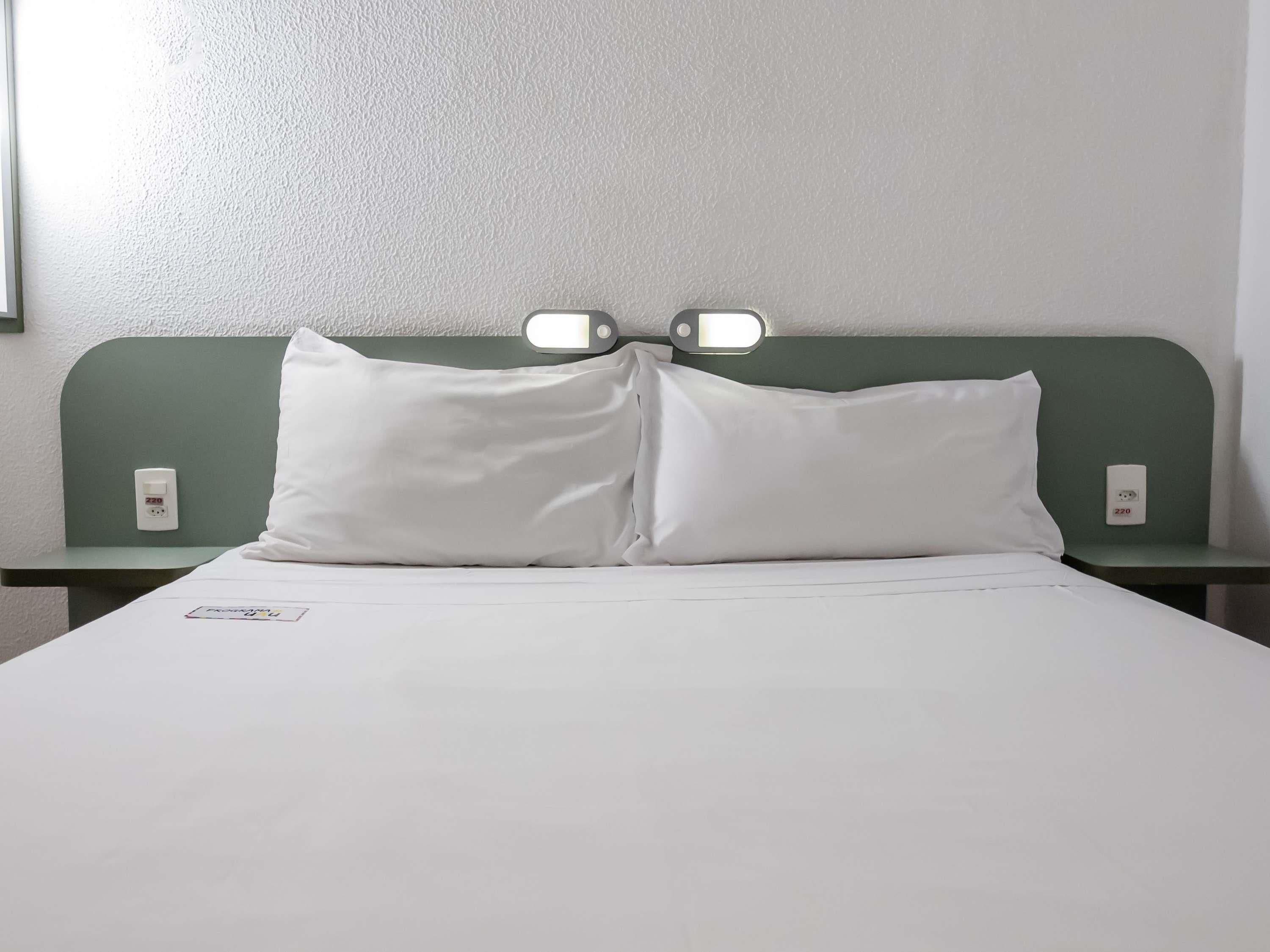 A hotel room with a single bed, two bedside tables, and a wall-mounted light fixture.