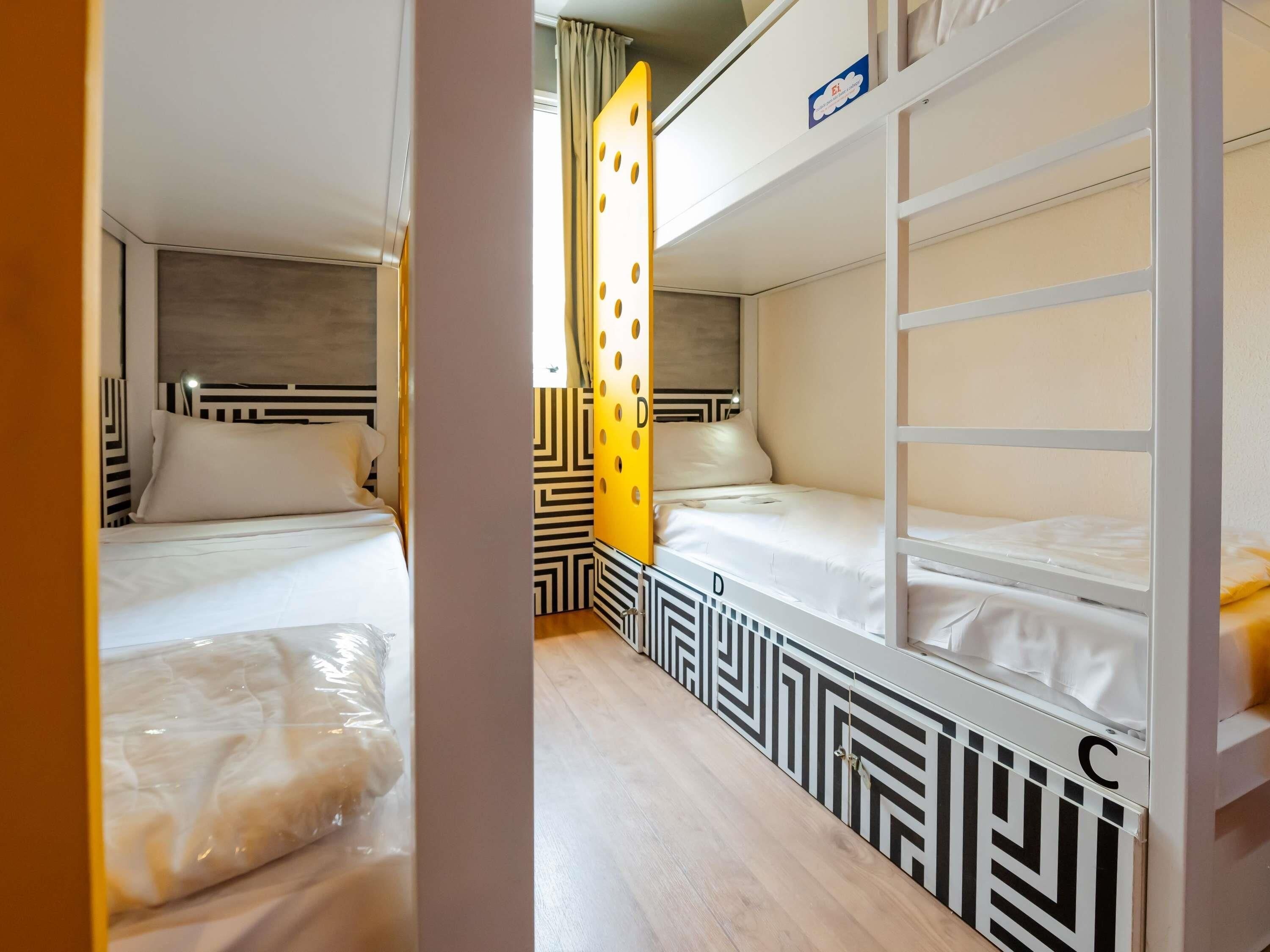 Une chambre d’hôtel avec des lits superposés, un mur à motifs et une fenêtre avec des rideaux.
