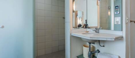 A bathroom with a shower, a sink, a mirror, and a towel rack.