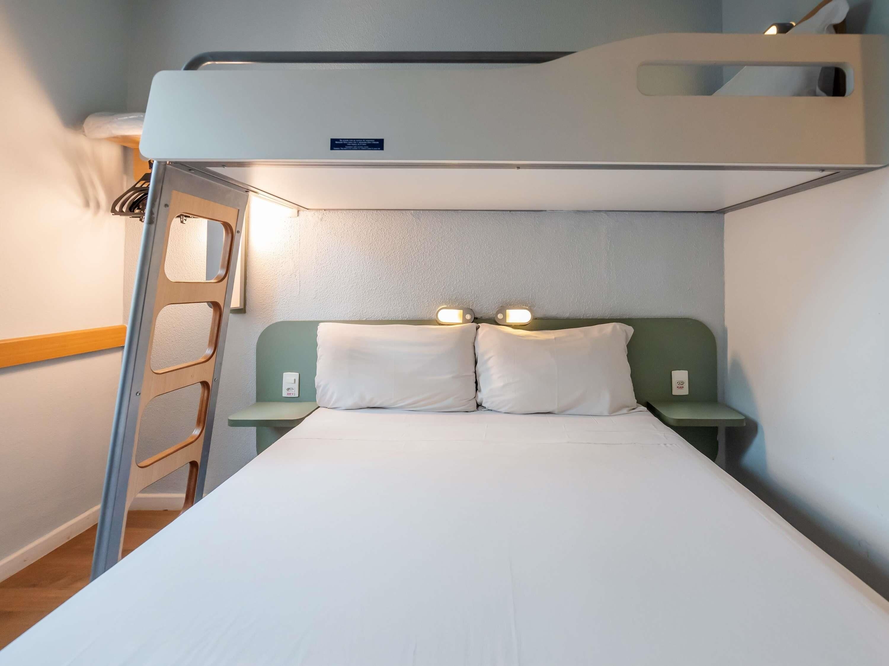 A bunk bed with a ladder, two bedside tables, and a headboard with built-in lighting.