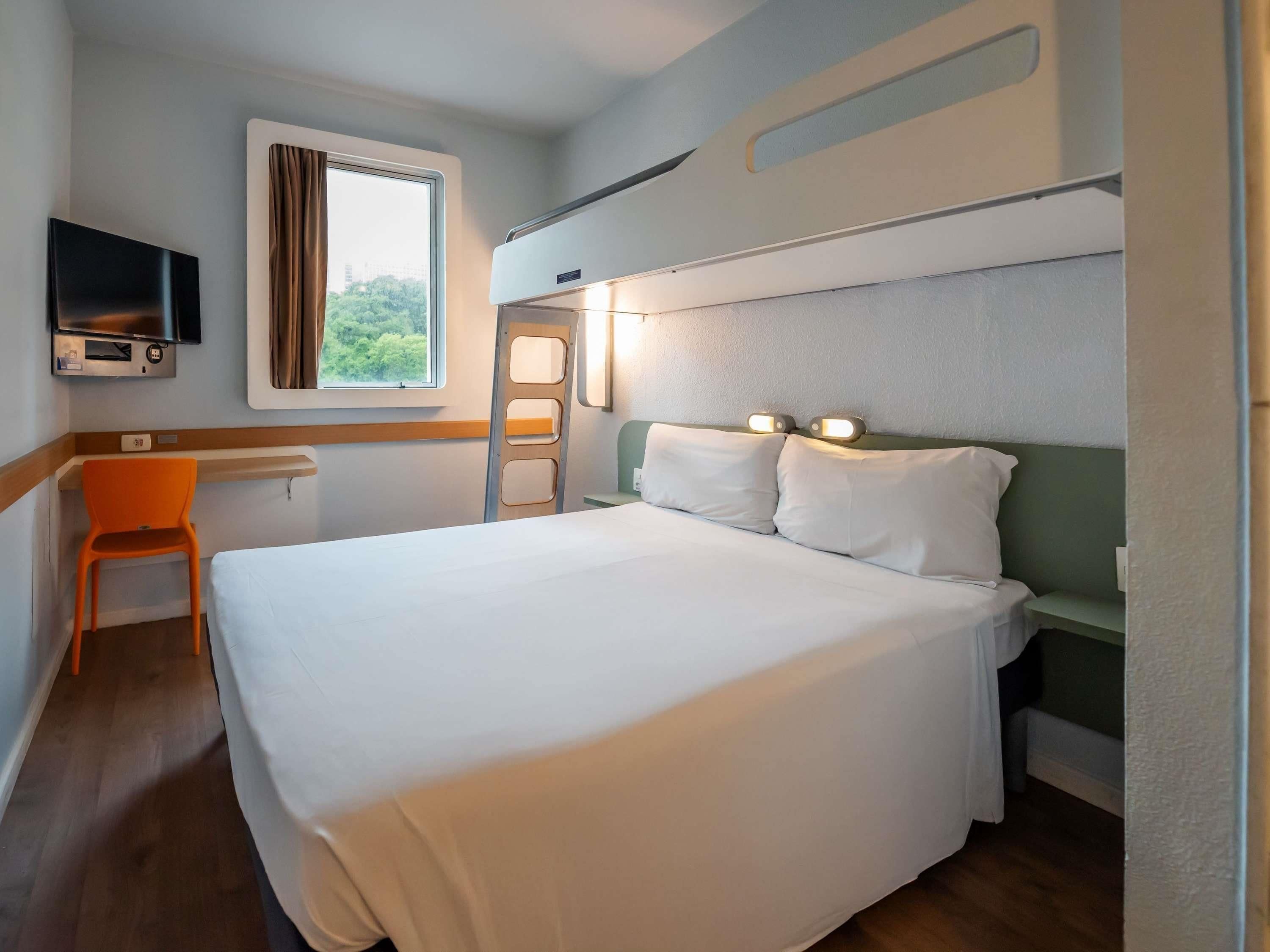 Une chambre d’hôtel équipée d’un lit, d’un bureau, d’une chaise, d’une télévision et d’une fenêtre avec des rideaux.