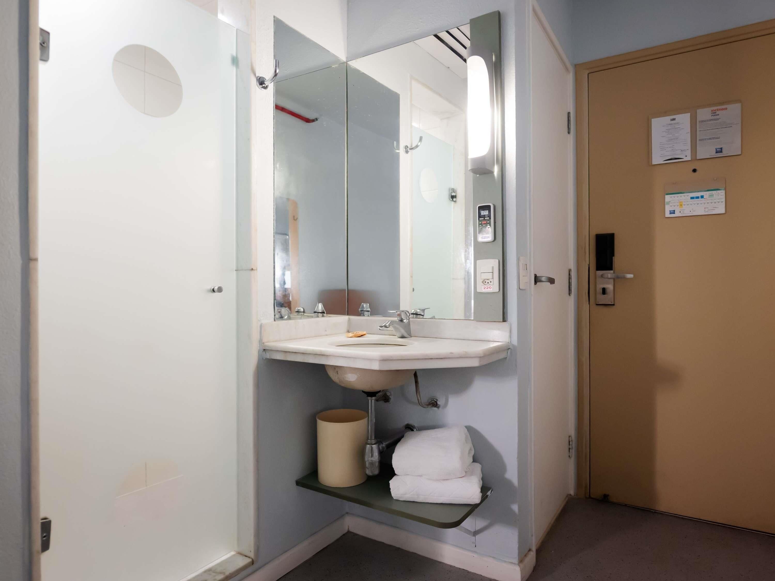 A hotel bathroom with a sink, mirror, towel rack, and a toilet paper holder.