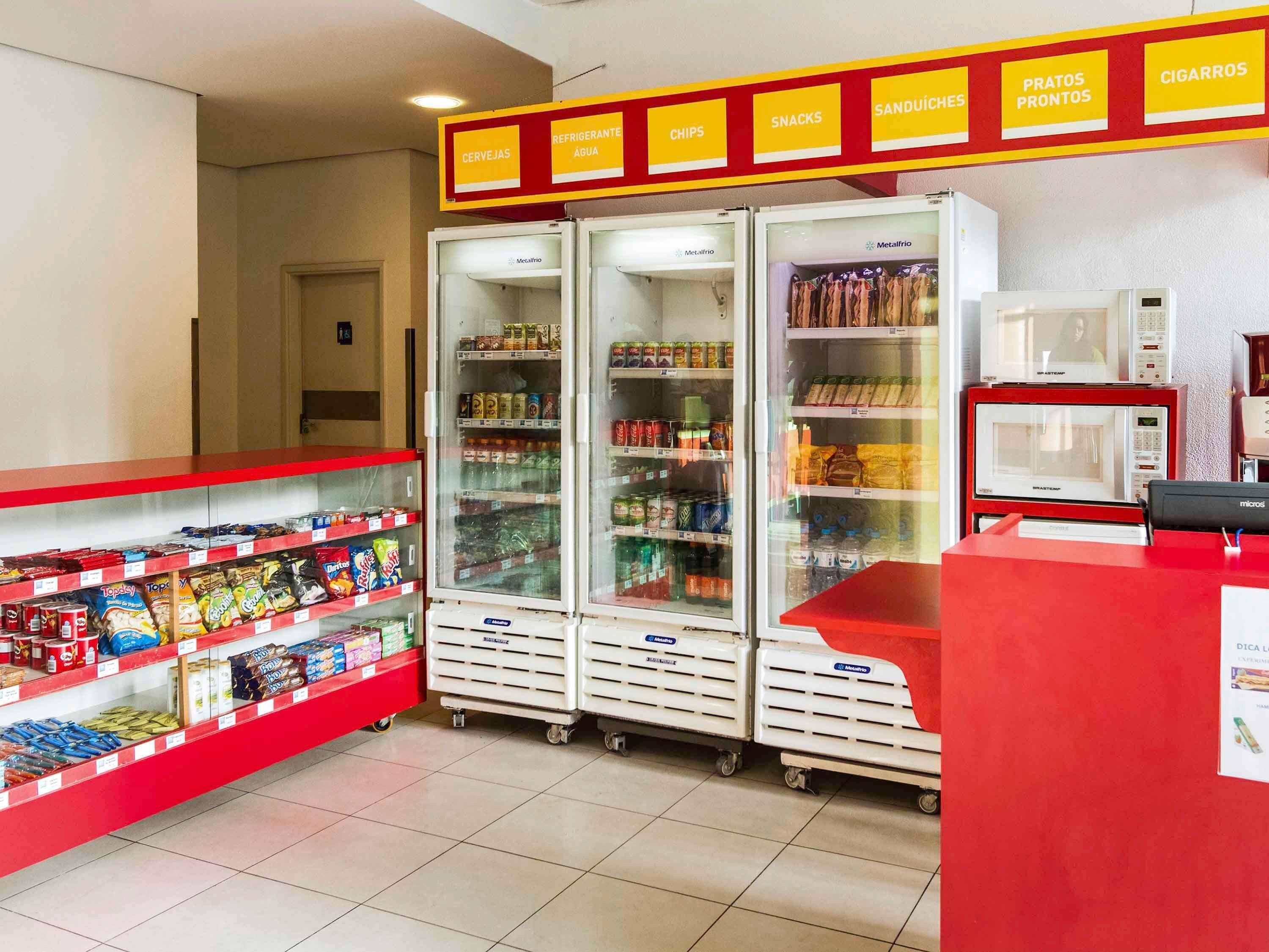 Un negozio di alimentari con reparti refrigerati e non, scaffali per snack e bevande, e un forno a microonde.