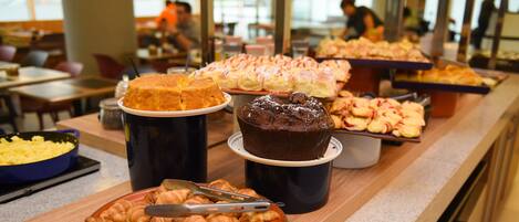 A buffet with various baked goods including pastries, cakes, and bread.