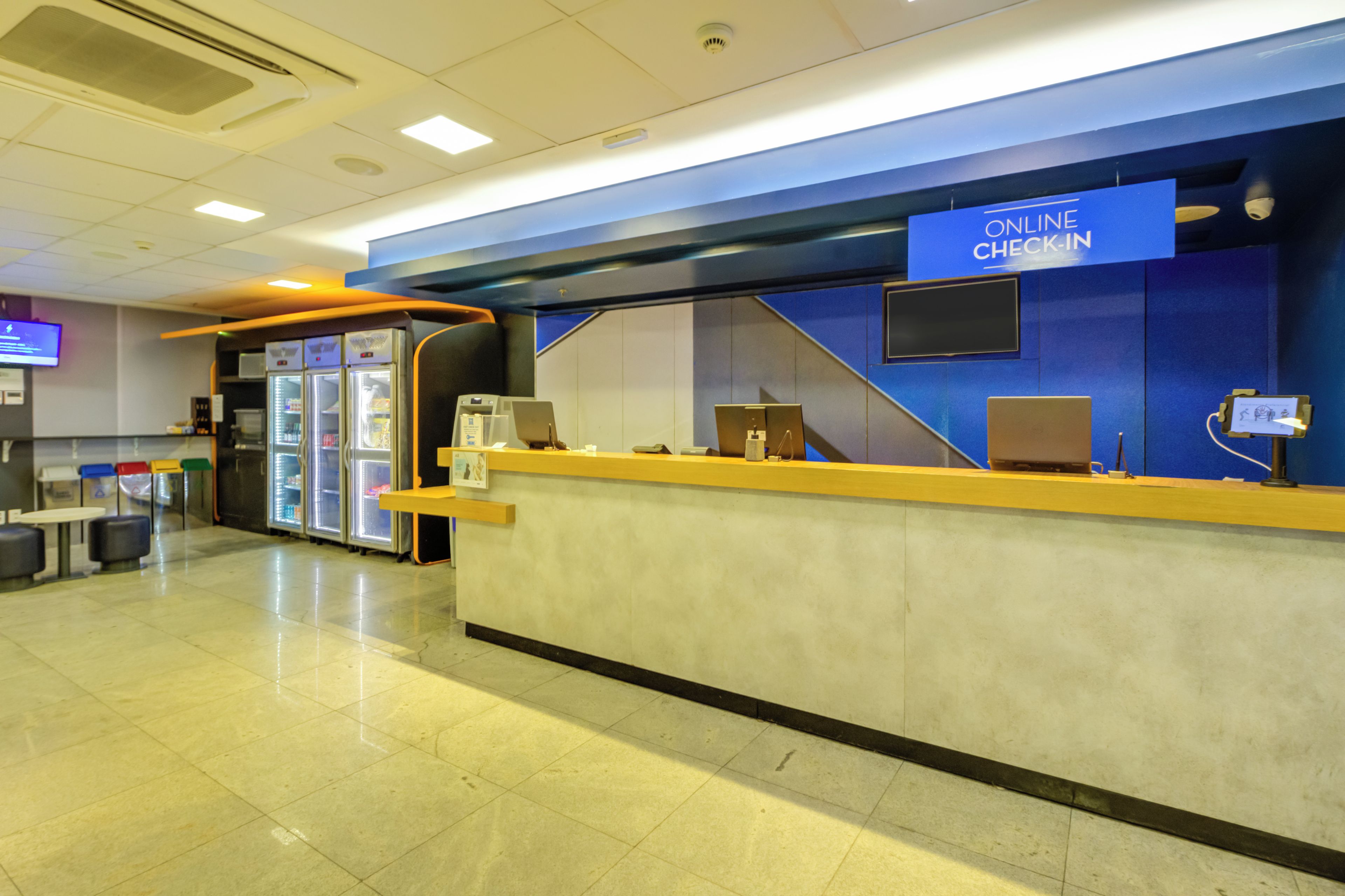 A check-in counter with an 'ONLINE CHECK-IN' sign, a seating area with chairs, and a refrigerator.