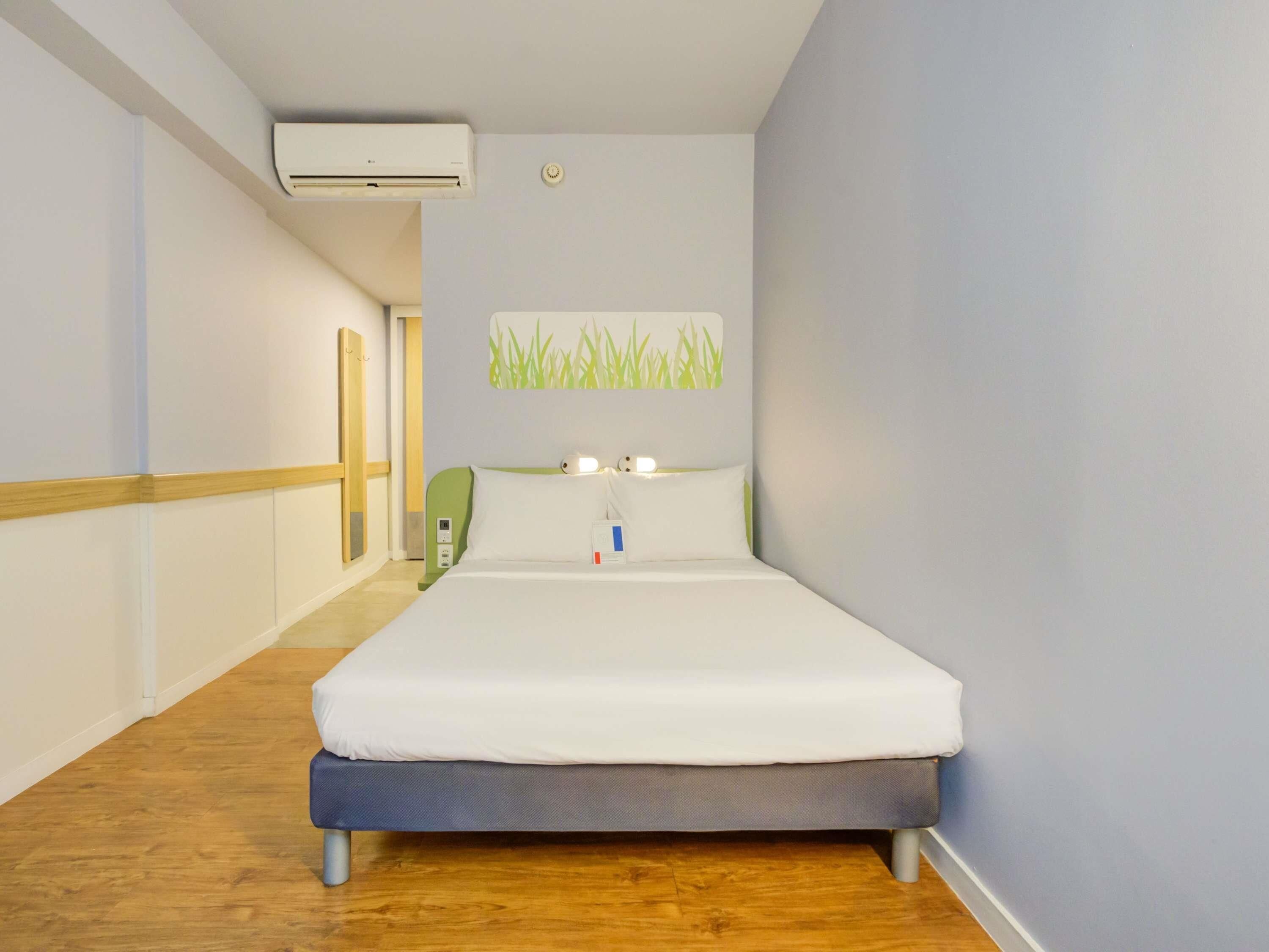 Habitación de hotel con cama, aire acondicionado de pared, mesita de noche y una obra de arte en la pared.