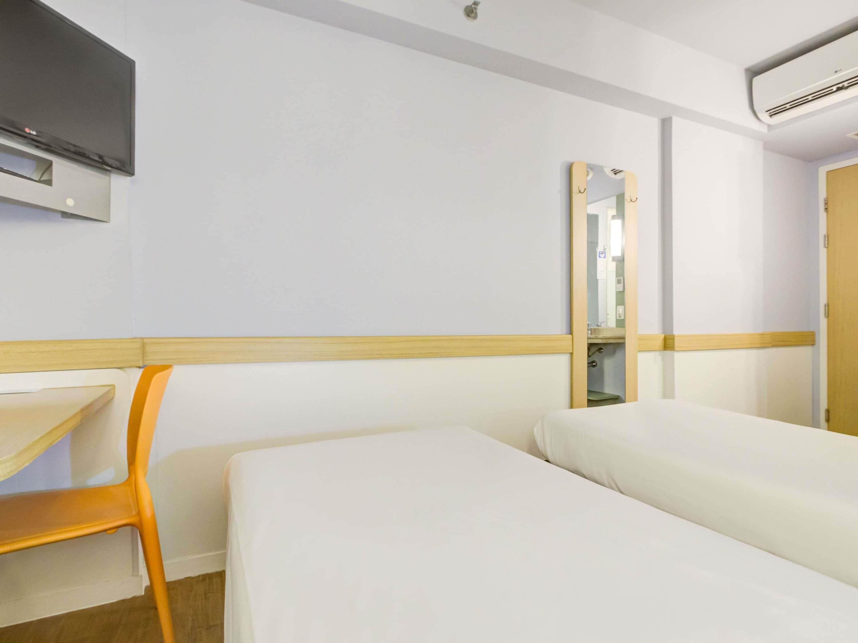 Una habitación de hotel con una cama, una silla, un televisor y un espejo.