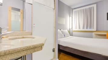 A hotel room with a bathroom, a bed, a nightstand, and a window with curtains.