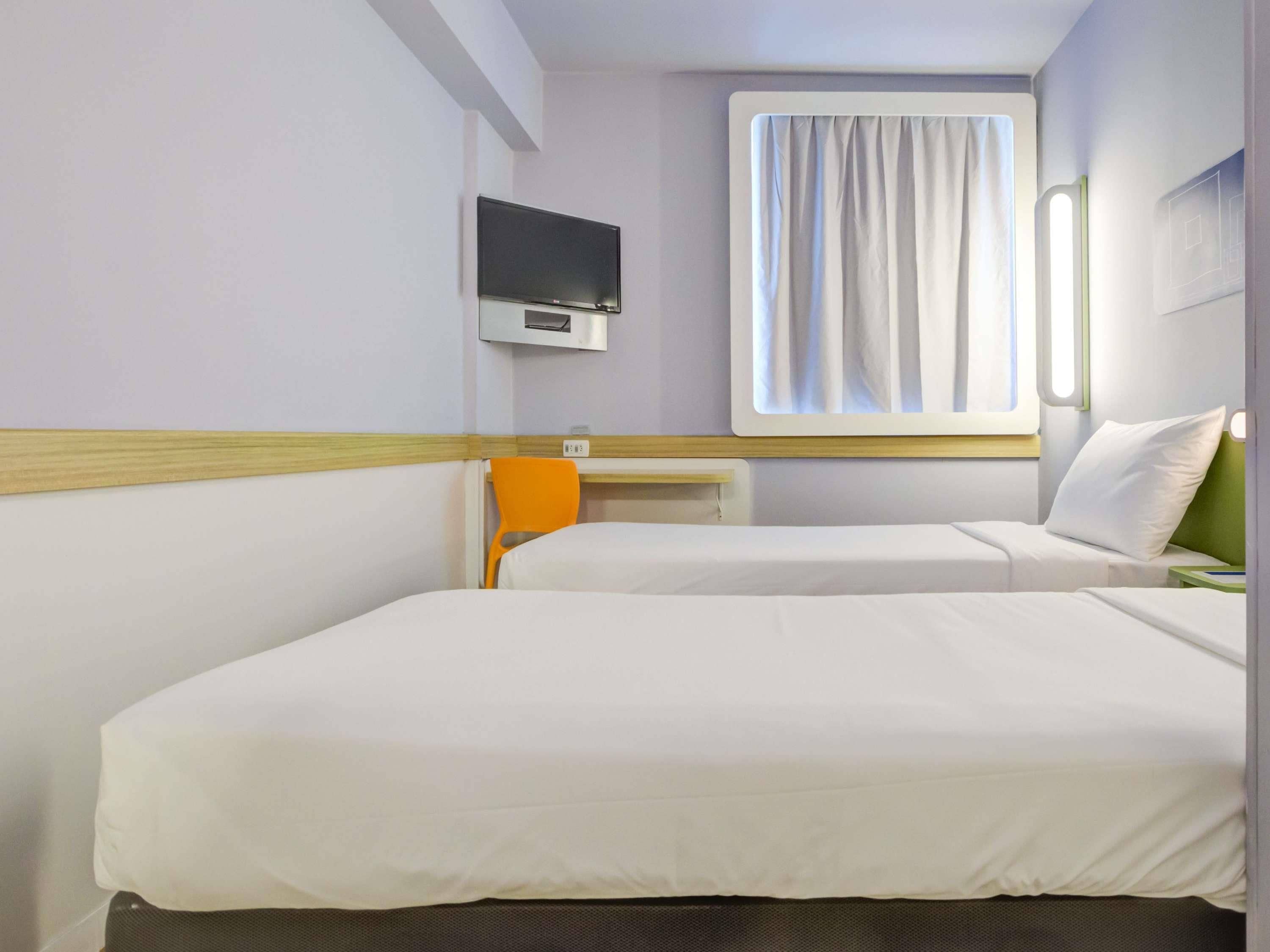 Habitación de hotel con dos camas, televisión, ventana con cortinas y una mesita.