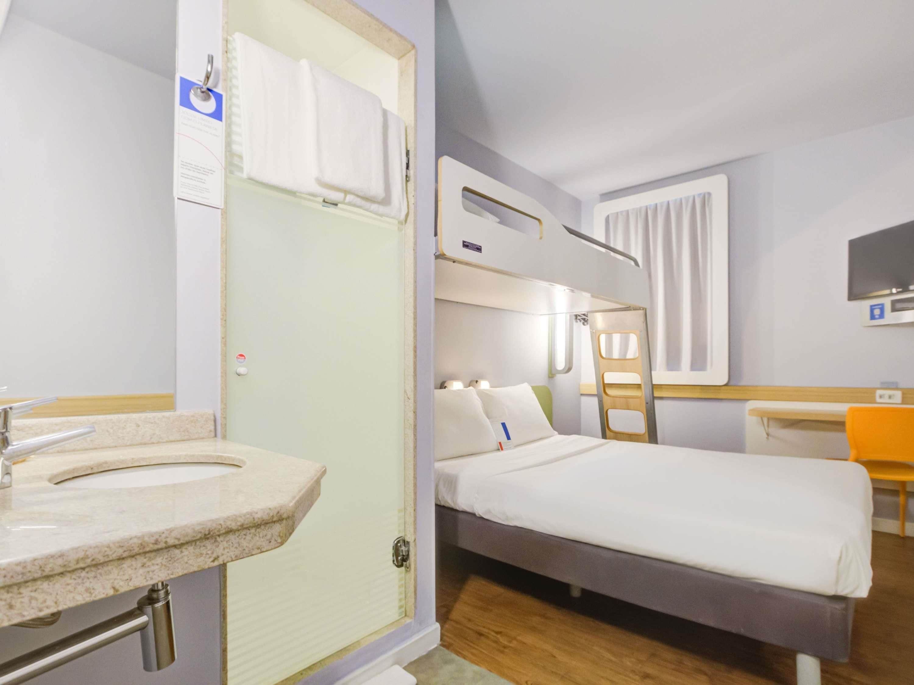 Una habitación de hotel con literas, un baño con lavamanos y espejo, un escritorio y un televisor.