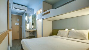 Quarto de hotel com beliches, mesa de cabeceira, espelho e ar condicionado.