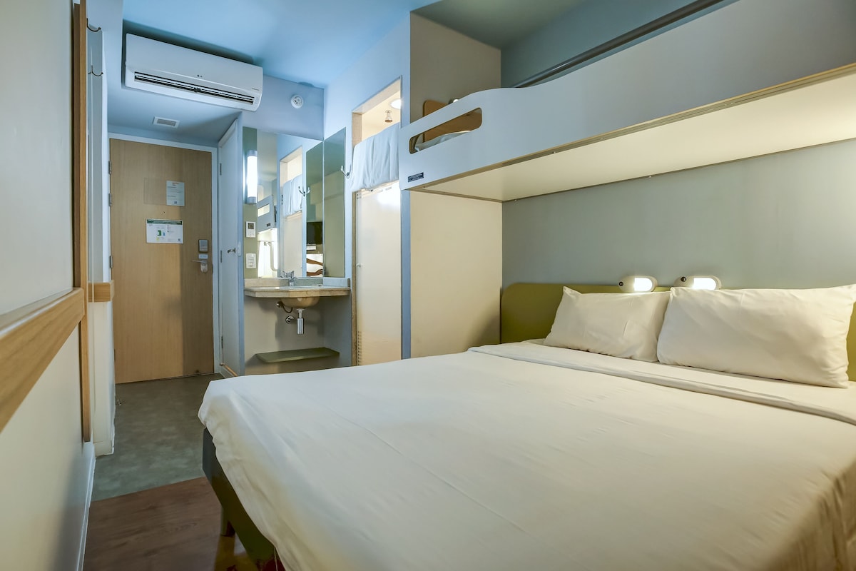 A hotel room with bunk beds, a bedside table, a mirror, and an air conditioning unit.