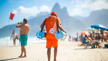 A beach scene with a person in orange attire carrying two blue buckets.