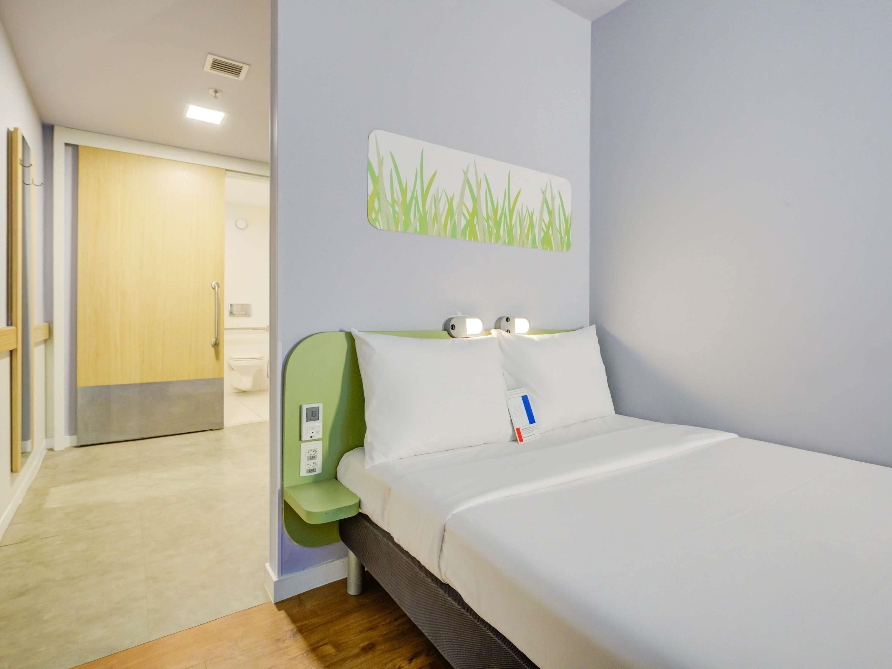 A hotel room with a bed, bedside table, and a wall-mounted light fixture.