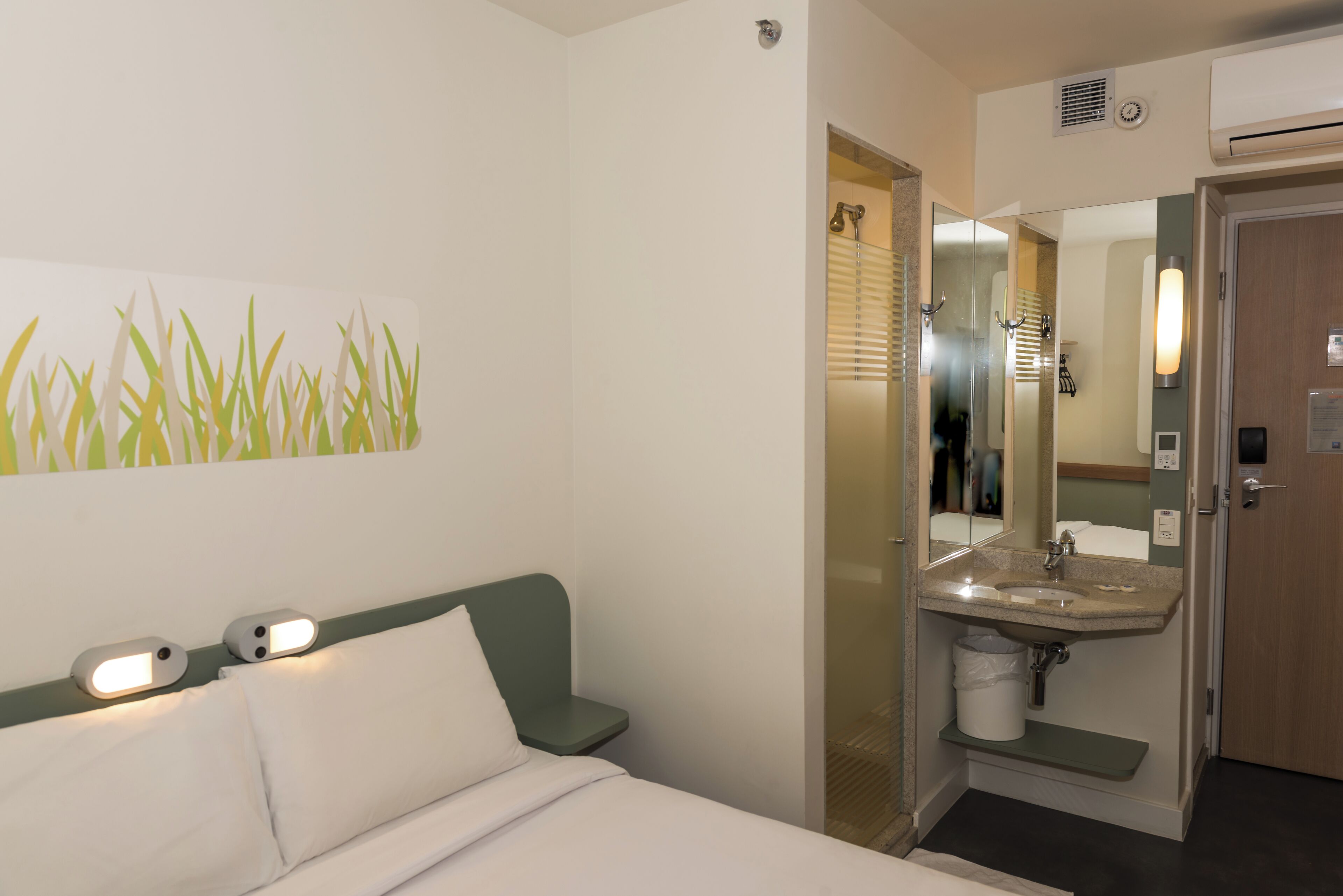 A hotel room with a bed, a bathroom with a sink and mirror, and a wall-mounted artwork.
