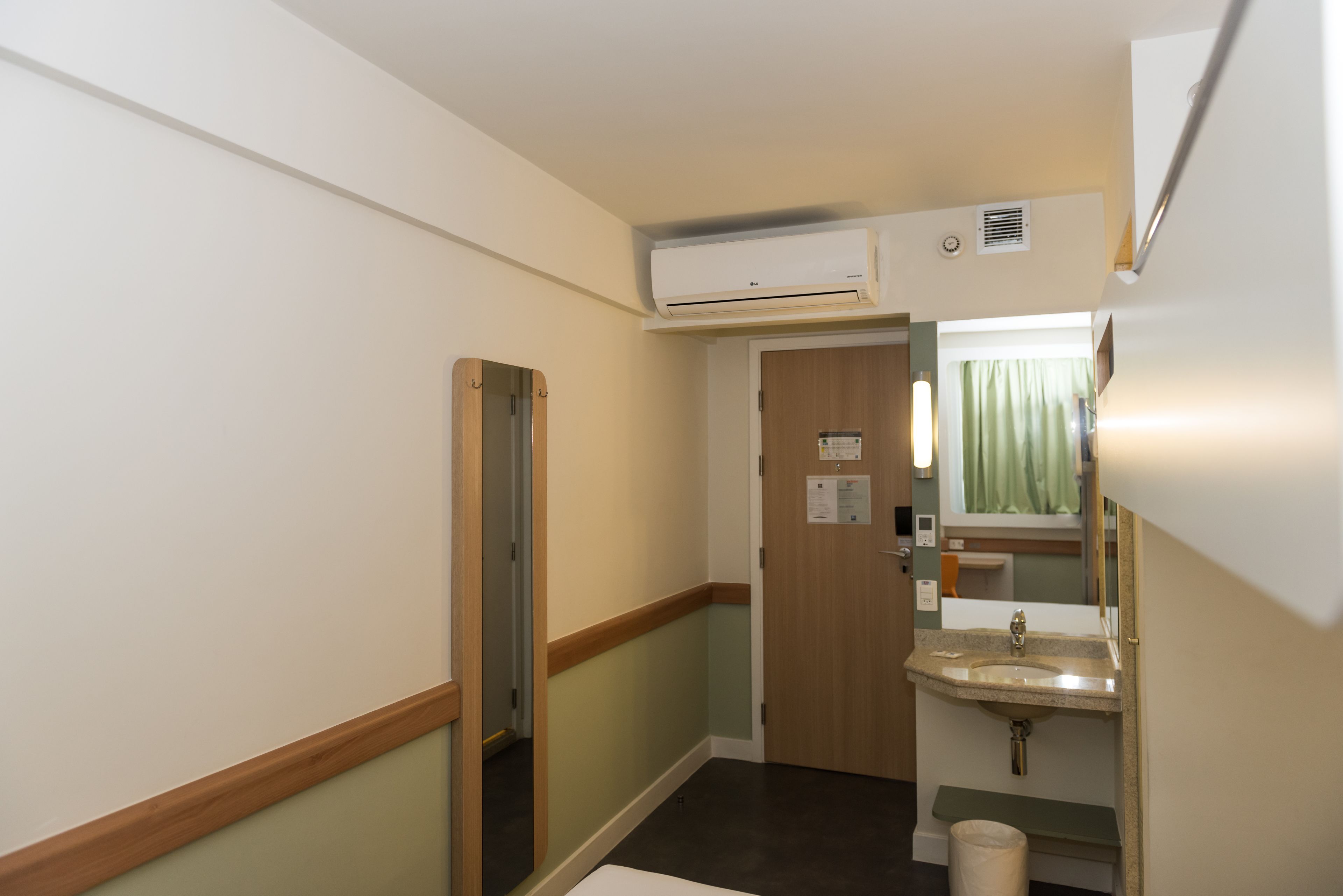 Un pasillo estrecho con una puerta de madera, un lavabo y un equipo de aire acondicionado.