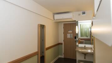 A narrow hallway with a wooden door, a sink, and an air conditioning unit.
