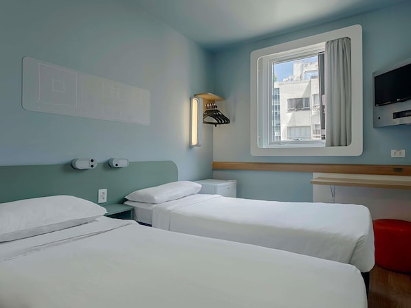 A hotel room with two beds, a TV, a window with curtains, a wall-mounted heater, and a wall-mounted light. - ibis budget RJ Praia de Botafogo (Rio de Janeiro)