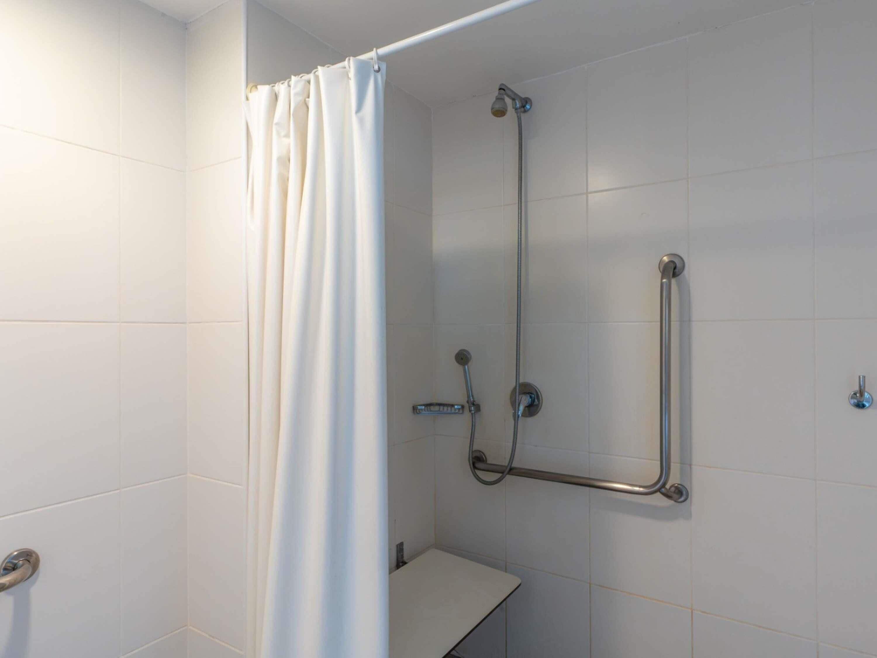 A shower with a white curtain, a handheld showerhead, and a grab bar.