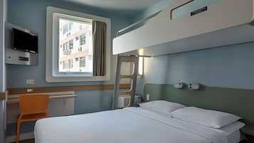 A hotel room with a bunk bed, a desk with a chair, a television, and a window with curtains.