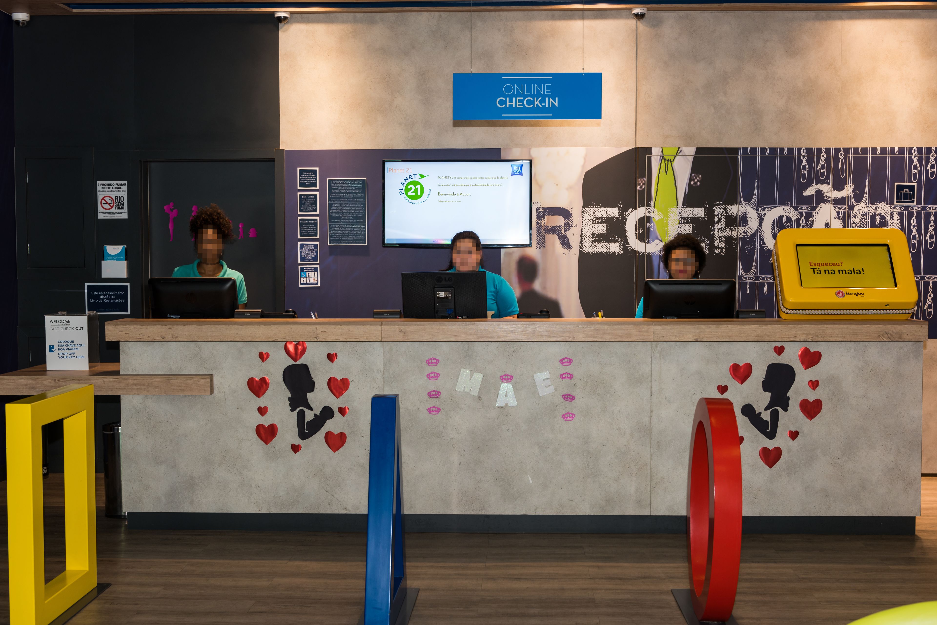 A reception desk with a digital screen displaying a message, a sign for online check-in, and a wall with a heart-themed design.
