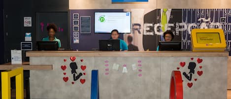 A reception desk with a digital screen displaying a message, a sign for online check-in, and a wall with a heart-themed design.