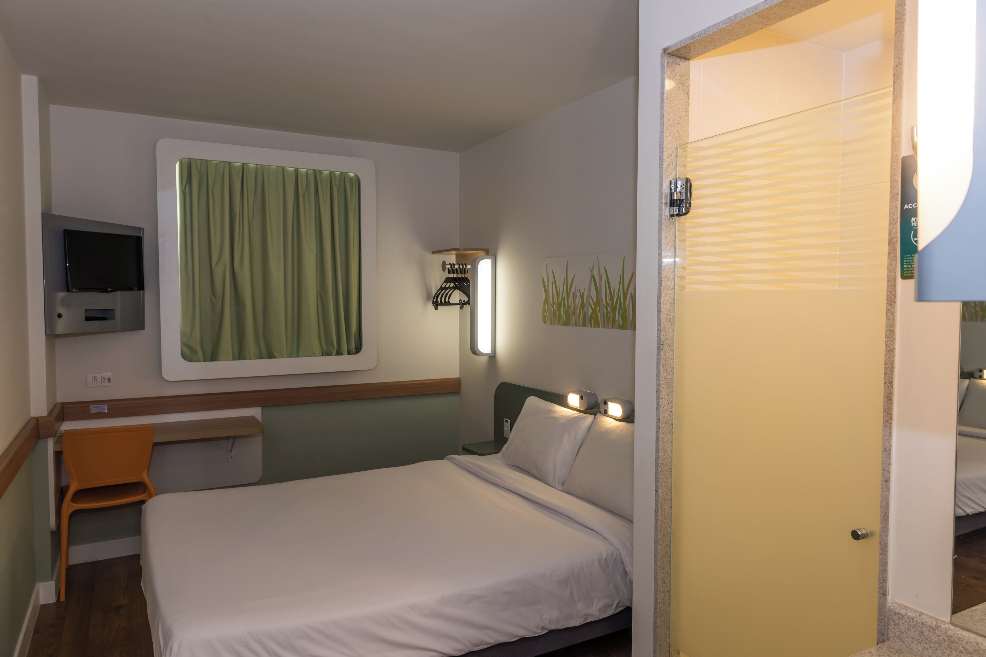 A hotel room with a bed, a desk, a television, and a window with curtains.