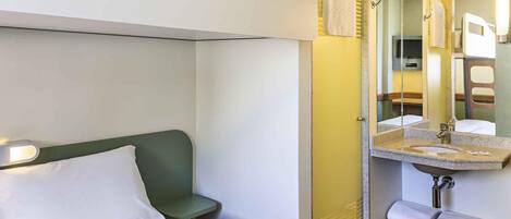 A hotel room with a bed, a green chair, a bathroom with a sink and mirror, and a shower area.