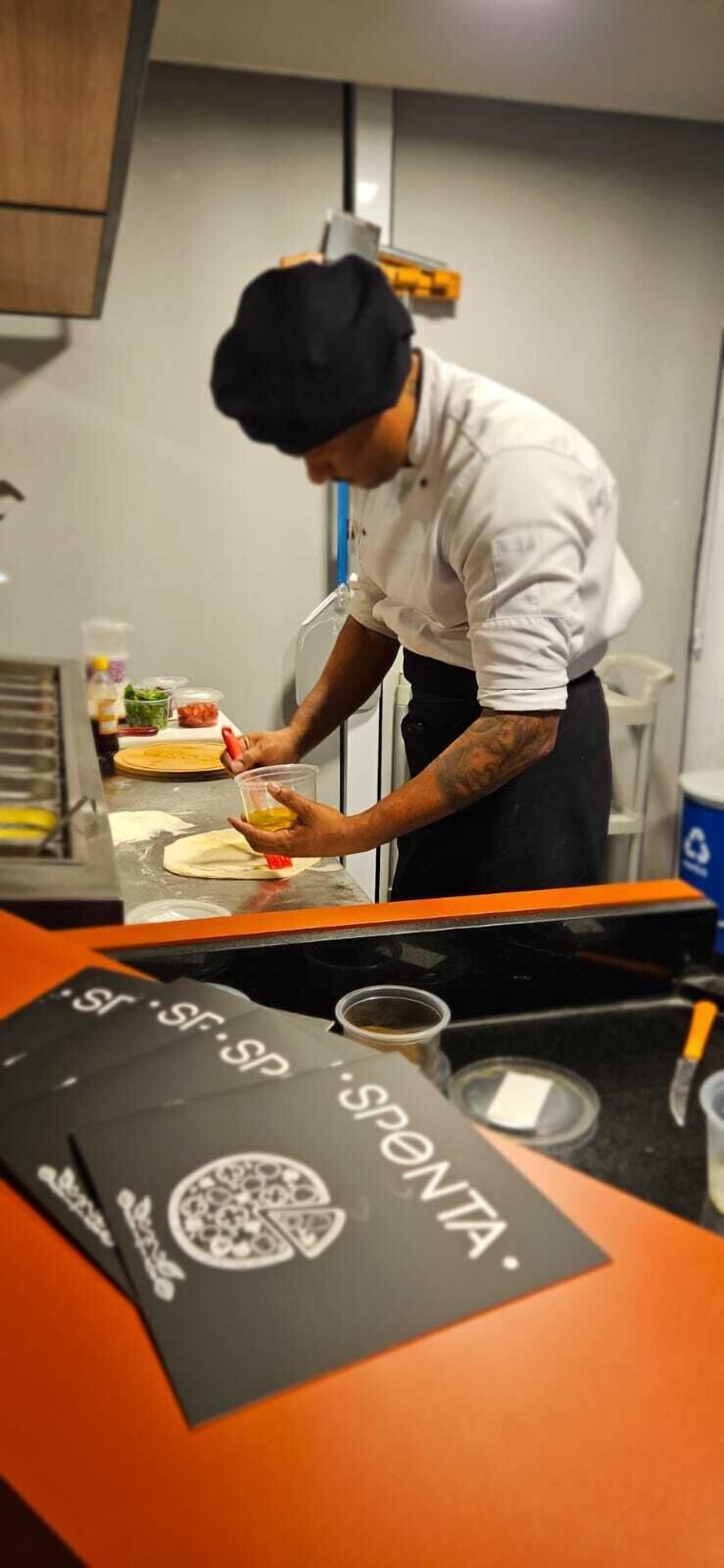 A chef preparing food in a kitchen with a black countertop and a menu stand.