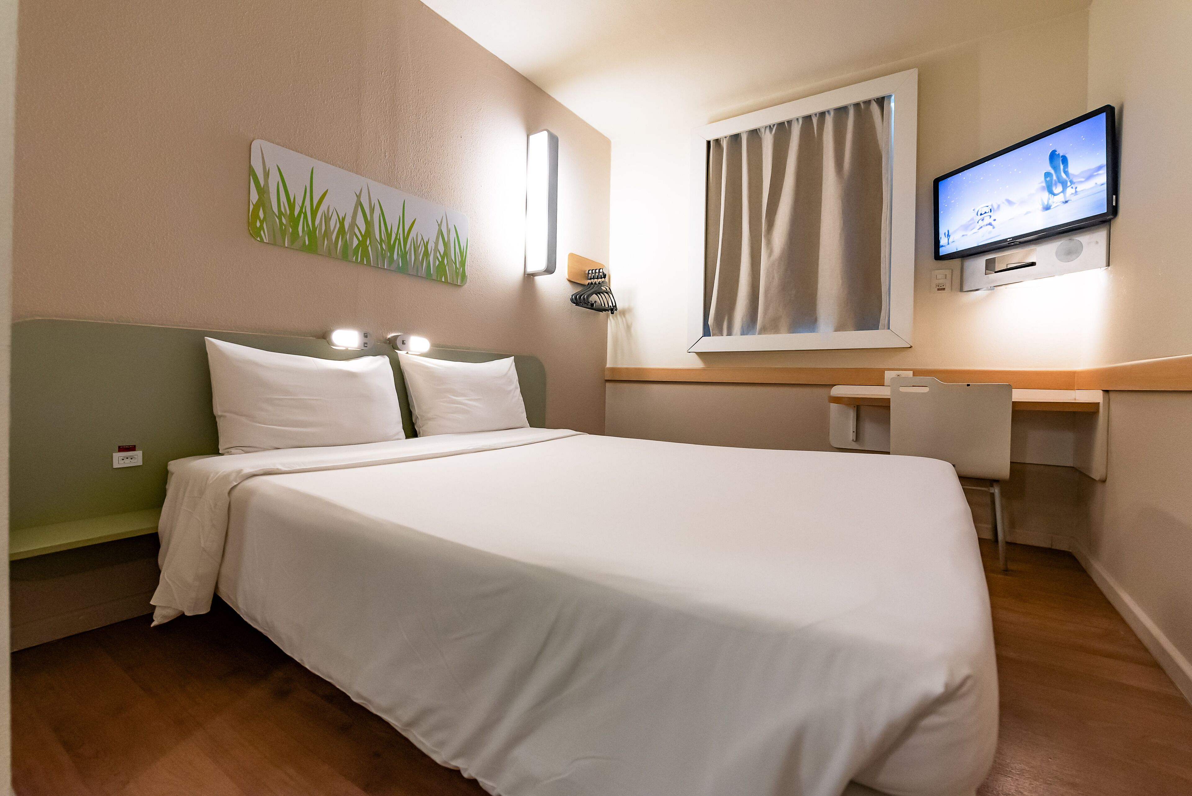 Une chambre d’hôtel avec un grand lit, un bureau, une télévision et une fenêtre avec des rideaux.