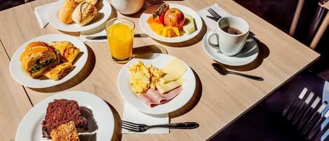 Una mesa de desayuno con varios platos, un vaso de zumo de naranja y una taza de café.