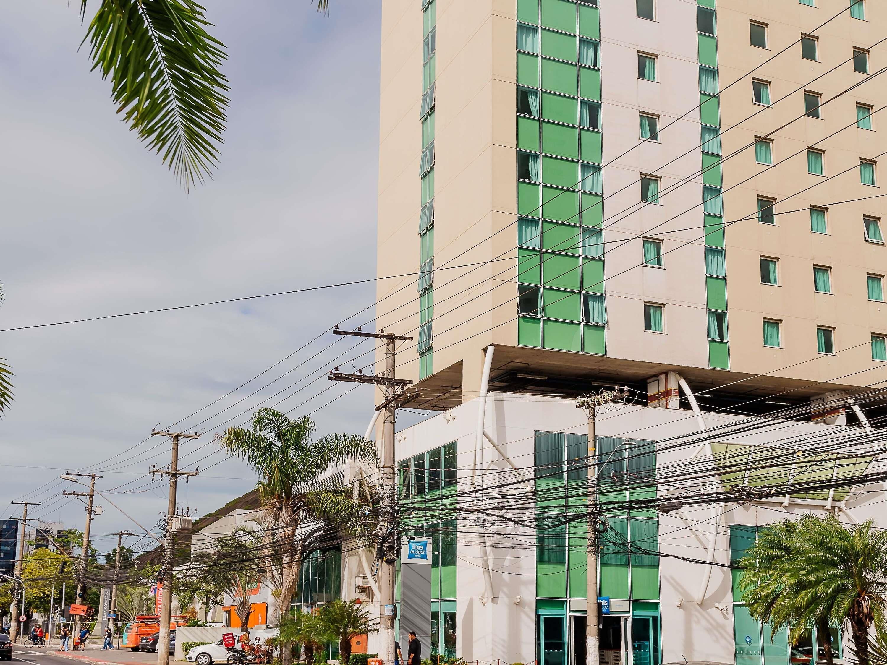 Un edificio de varios pisos con un diseño arquitectónico moderno, que destaca por su fachada verde y numerosos ventanales.